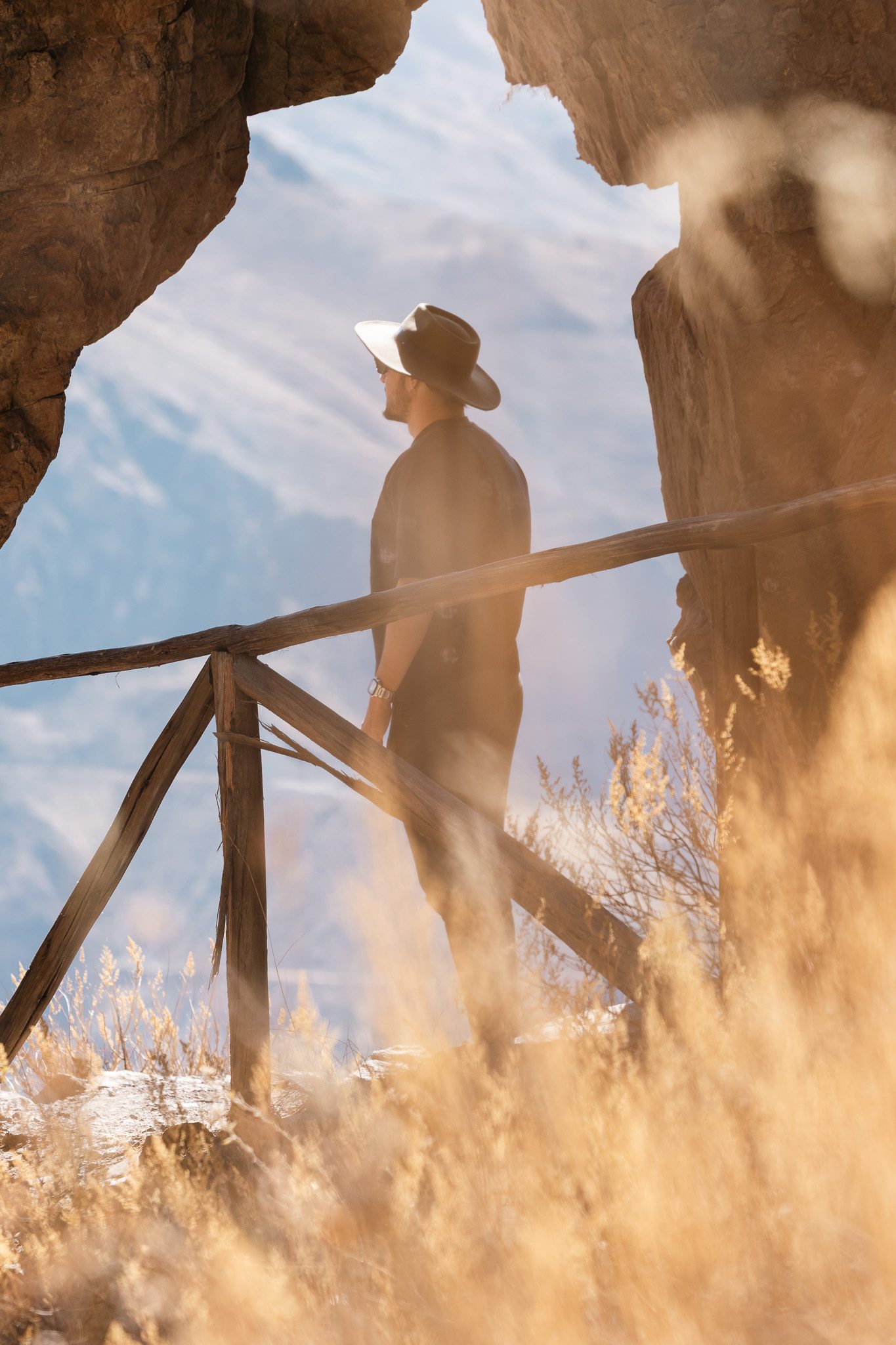 Traveler standing at a wooden lookout framed by rock formations in a mountainous landscape.
