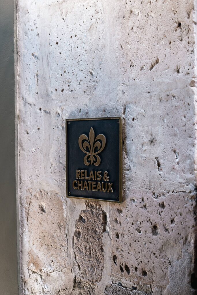 Close-up of a Relais & Chateaux metal plaque on a textured stone wall.